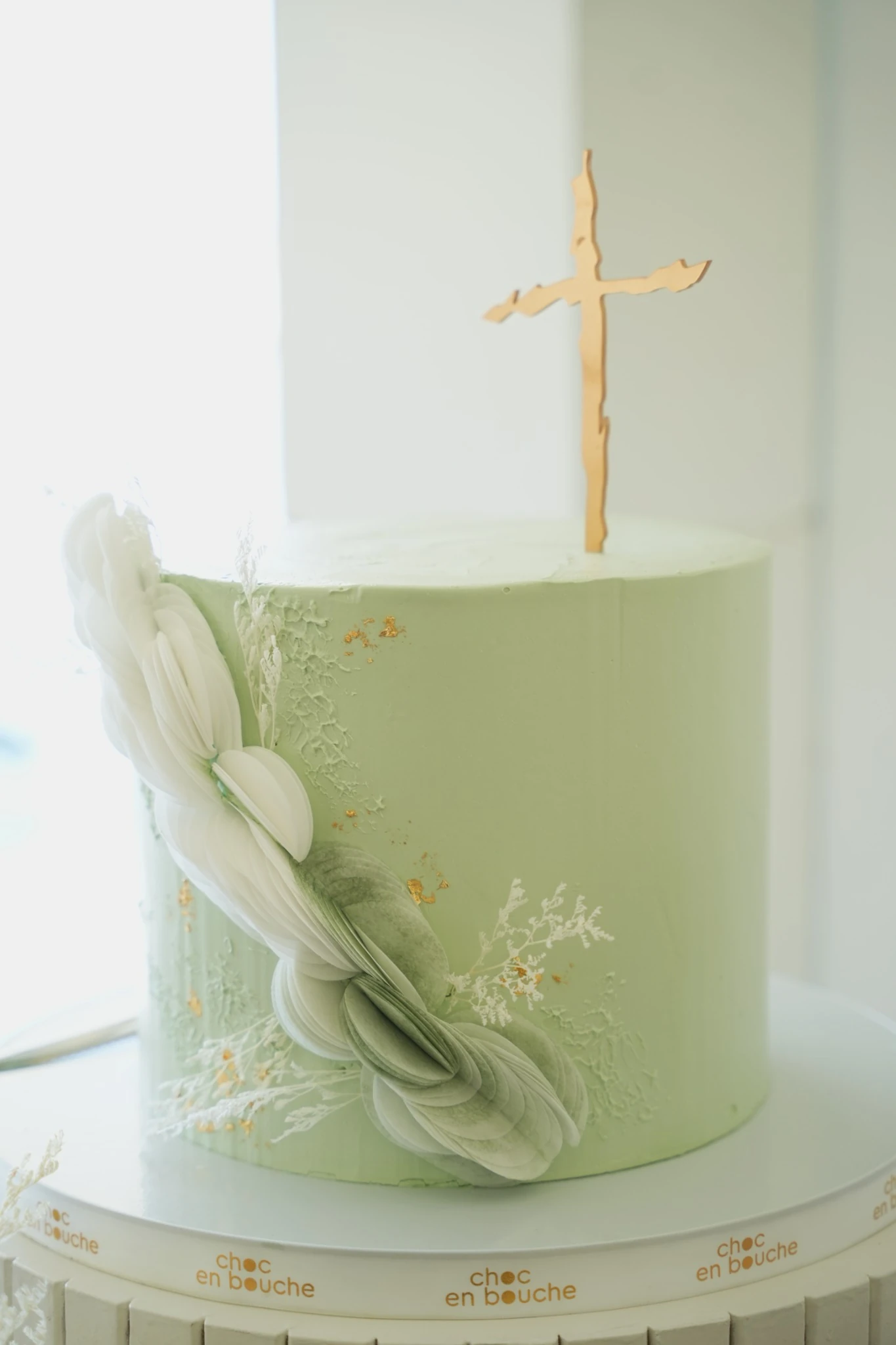 Pale green baptism cake with delicate sugar florals and a gold cross