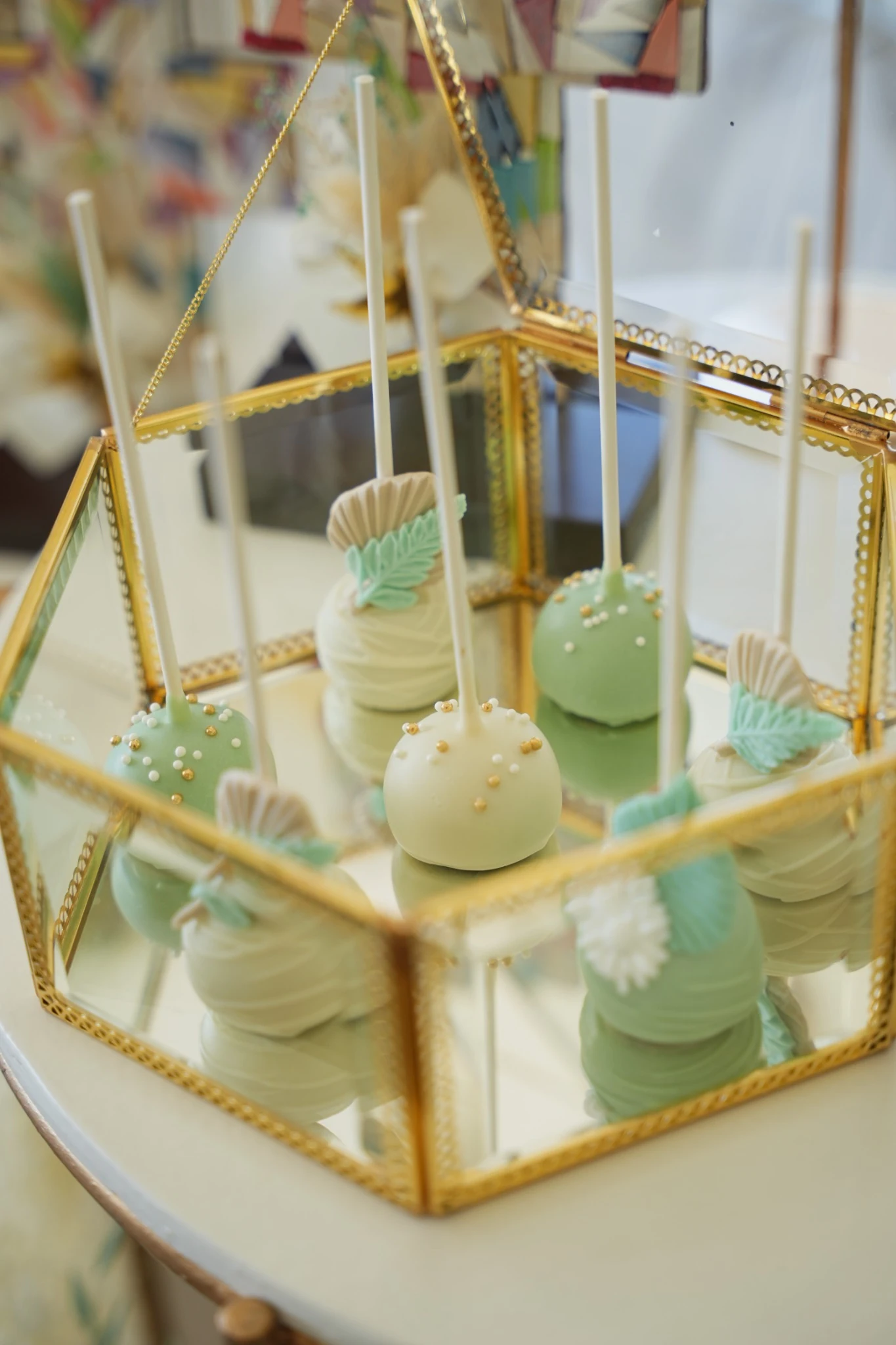 Mint green and ivory baptism cake pops arranged in a gold glass display box
