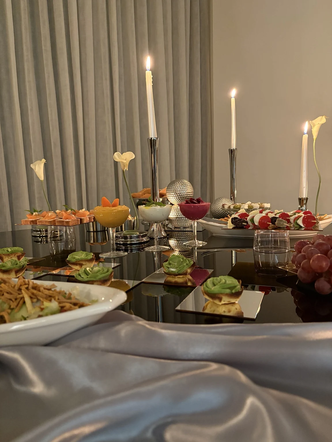 Wide view of the buffet with silver fabric draping and lit tapered candles
